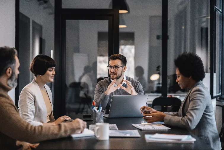 Colleagues discussing around a meeting table with a laptop